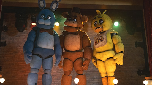 One of many frames taken from the ‘Five Nights at Freddy’s’ movie, displaying the main three (Bonnie the Bunny, Freddy the Bear, and Chica the Chicken) on stage.